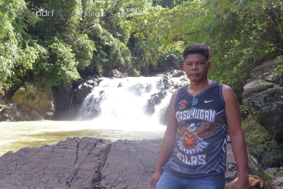 A community member stands beside a waterfall during field validation.